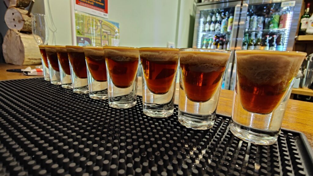 Shot of baby Guinness lined up on a bar ready for consumption. Baby Guinness is Tia Maria and Bailey's. The Bailey's is gently poured over a spoon so that it does not mix with the Tia Maria and instead sits on top and the light colour of the Bailey's make the shot look like a baby Guiness. Hence the name.