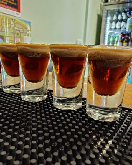 Shot of baby Guinness lined up on a bar ready for consumption. Baby Guinness is Tia Maria and Bailey's. The Bailey's is gently poured over a spoon so that it does not mix with the Tia Maria and instead sits on top and the light colour of the Bailey's make the shot look like a baby Guiness. Hence the name.