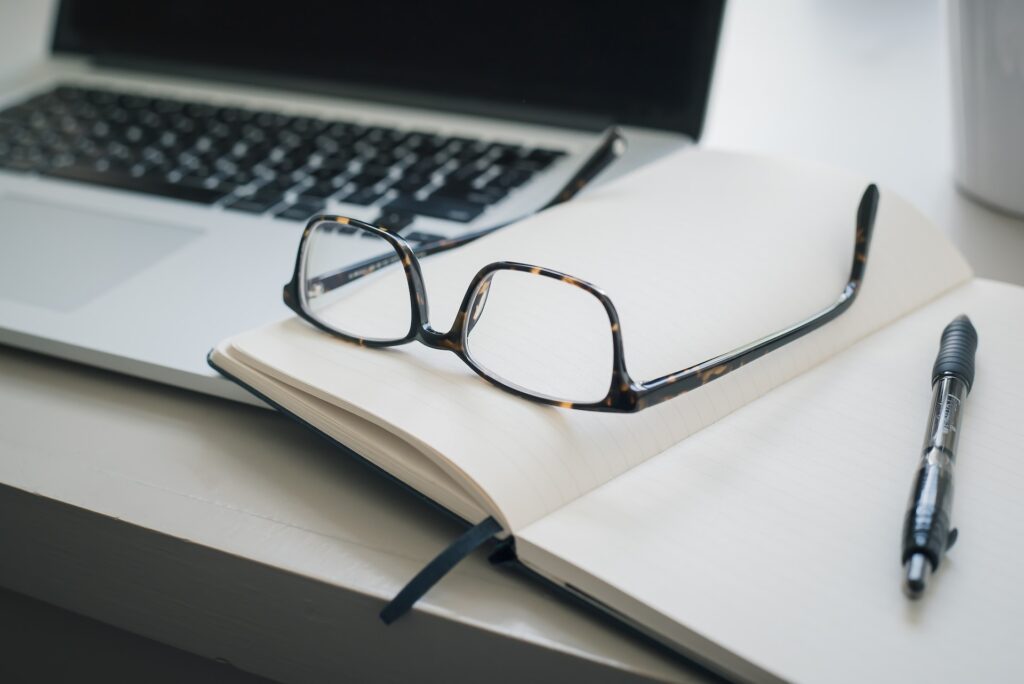 Computer on desk with notepad, pen and glasses